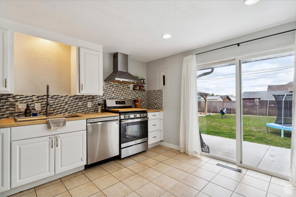 Kitchen featuring wall chimney range hood, decorative backsplash, appliances with stainless steel finishes, a sink, and butcher block counters