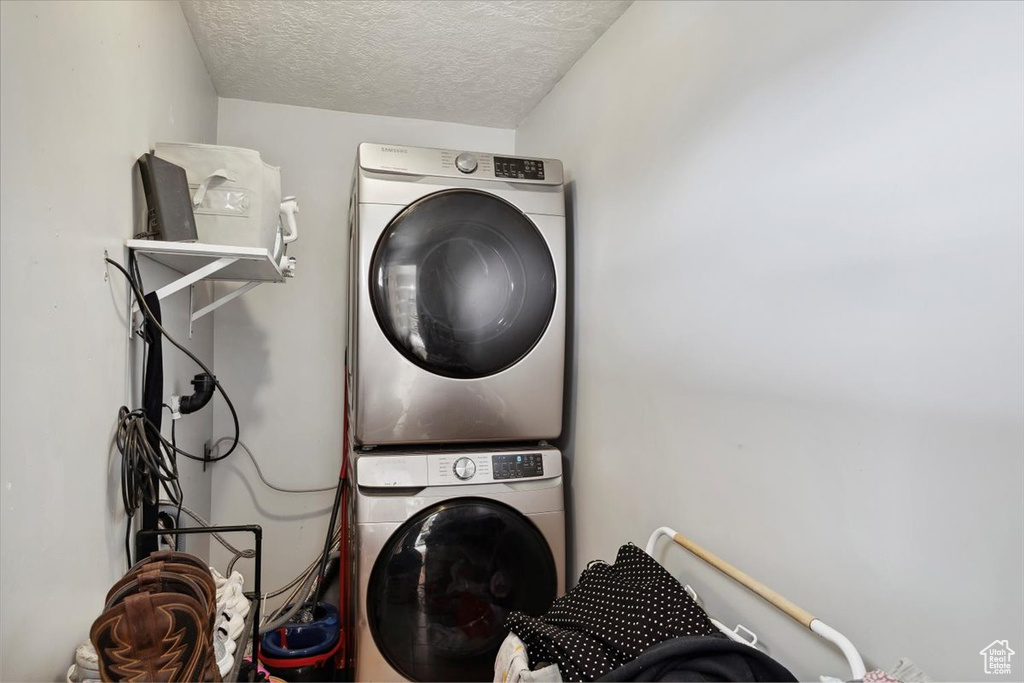 Washroom with laundry area, stacked washer and dryer, and a textured ceiling