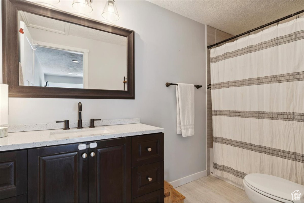 Full bathroom featuring vanity, toilet, a textured ceiling, a shower with shower curtain, and baseboards