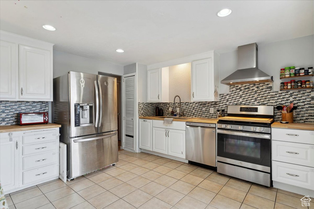 Kitchen featuring a sink, butcher block countertops, stainless steel appliances, and wall chimney exhaust hood