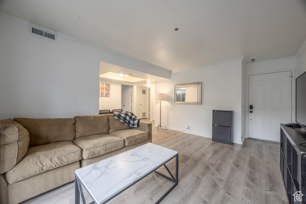 Living area with crown molding, baseboards, visible vents, and light wood-style floors