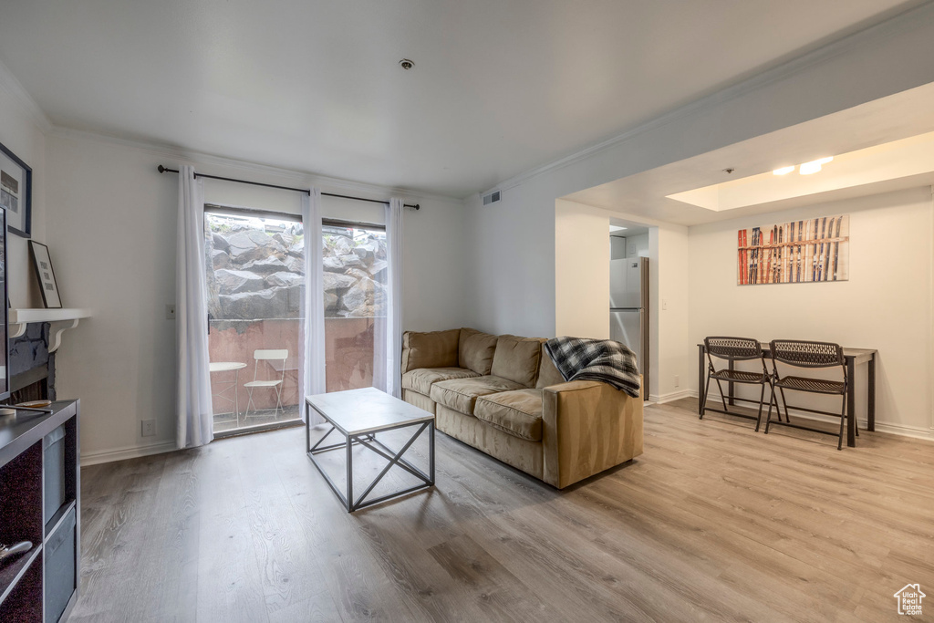 Living area featuring crown molding, light wood-style flooring, baseboards, and a skylight