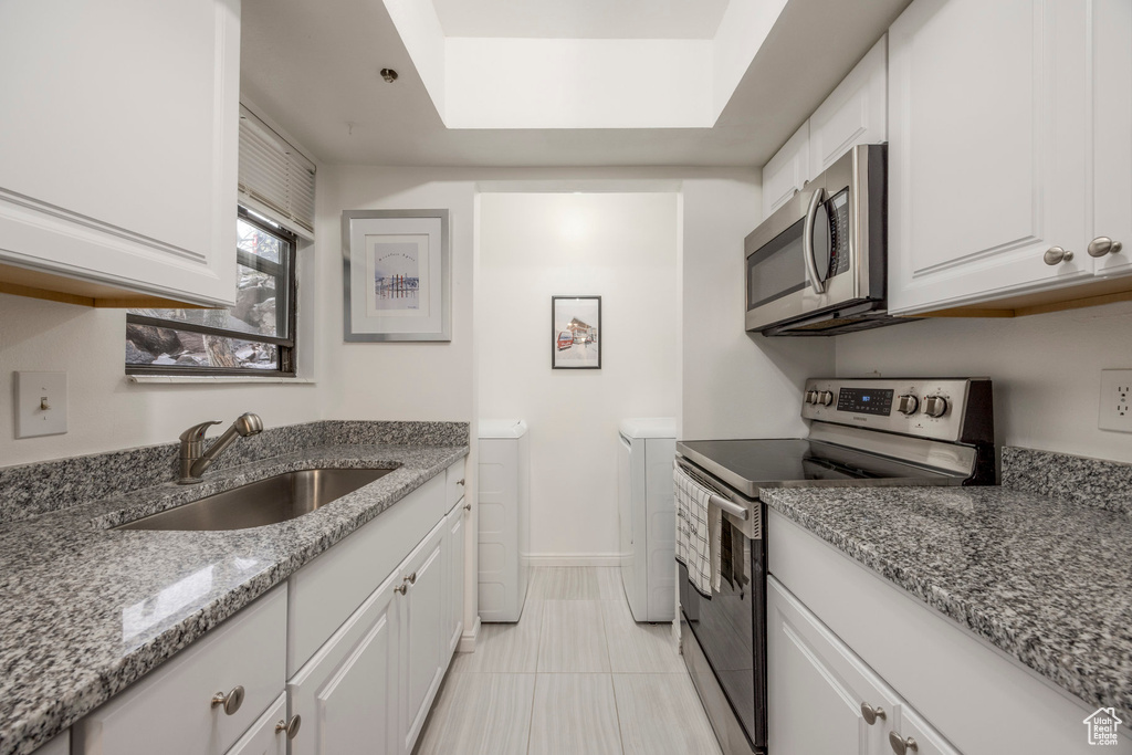 Kitchen with appliances with stainless steel finishes, a sink, white cabinets, light tile patterned flooring, and washer and dryer