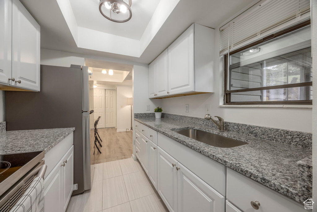 Kitchen featuring light stone countertops, a sink, a raised ceiling, white cabinets, and light tile patterned flooring