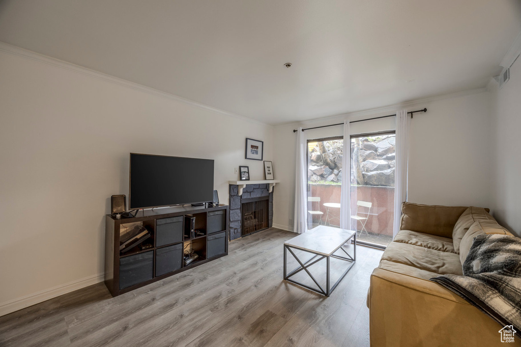 Living area with visible vents, crown molding, a fireplace, baseboards, and light wood-style floors