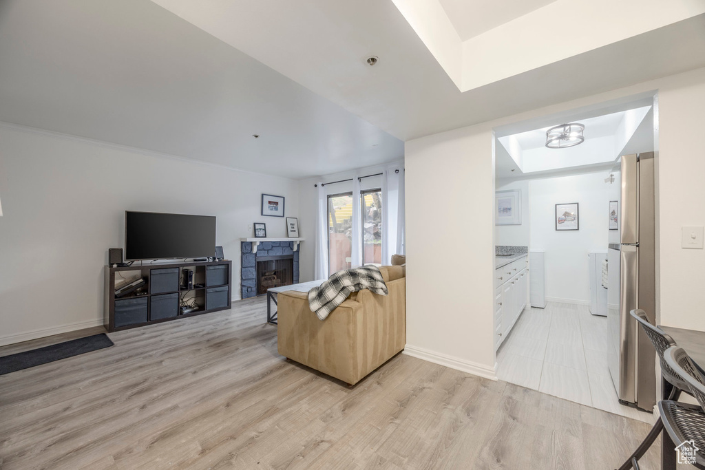 Living area featuring a skylight, a stone fireplace, baseboards, and light wood-style floors