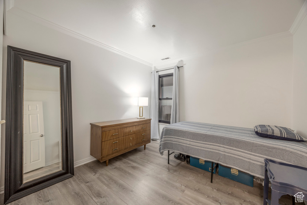Bedroom with baseboards, ornamental molding, light wood-style flooring, and visible vents