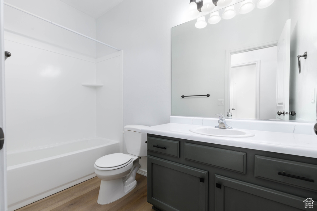 Bathroom featuring toilet,  shower combination, wood finished floors, and vanity