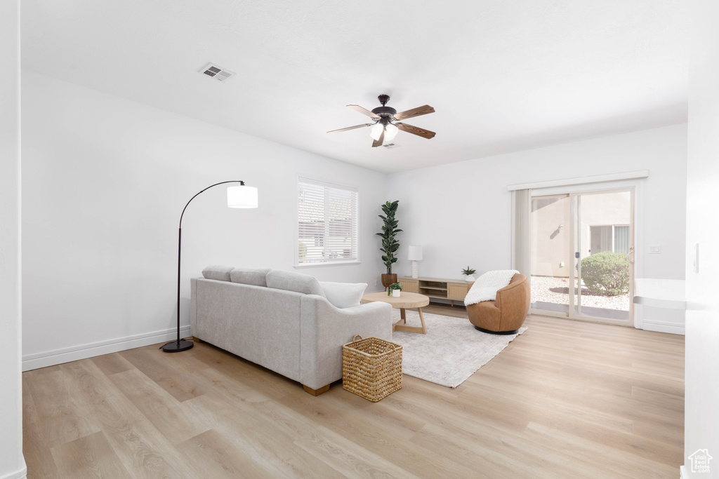 Living room with visible vents, light wood finished floors, ceiling fan, and baseboards