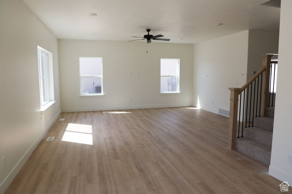 Unfurnished living room featuring visible vents, light wood-style floors, baseboards, ceiling fan, and stairway