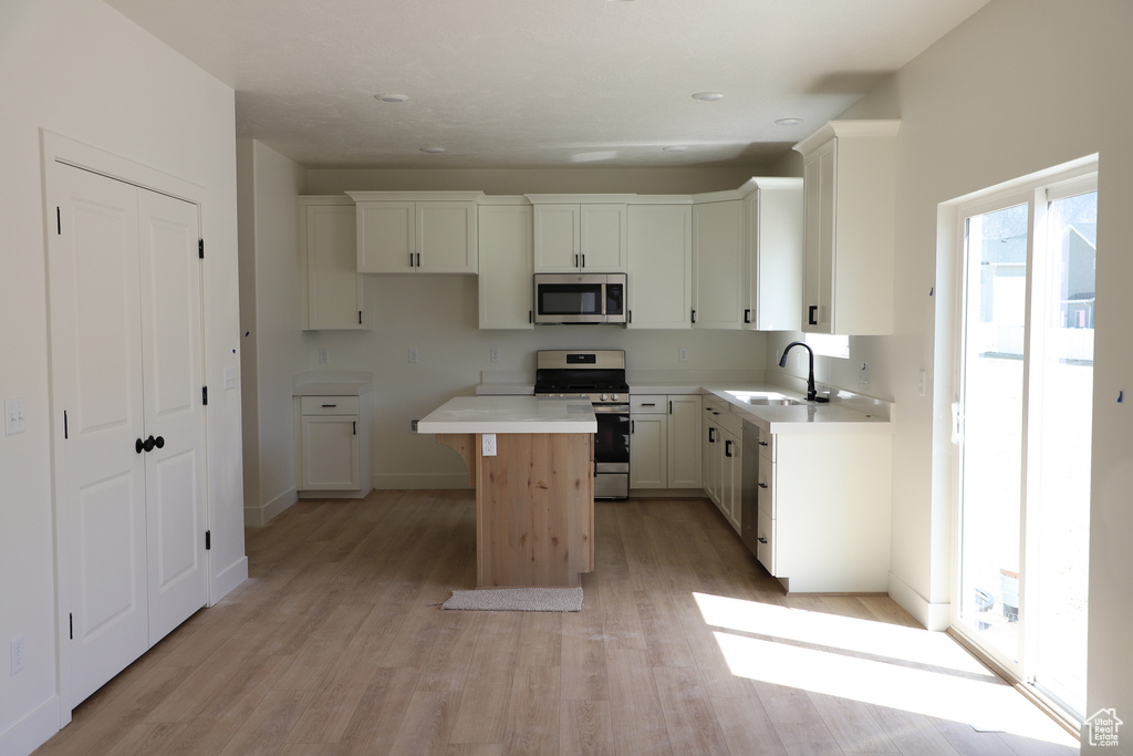 Kitchen featuring appliances with stainless steel finishes, a center island, a sink, white cabinets, and light wood-style floors