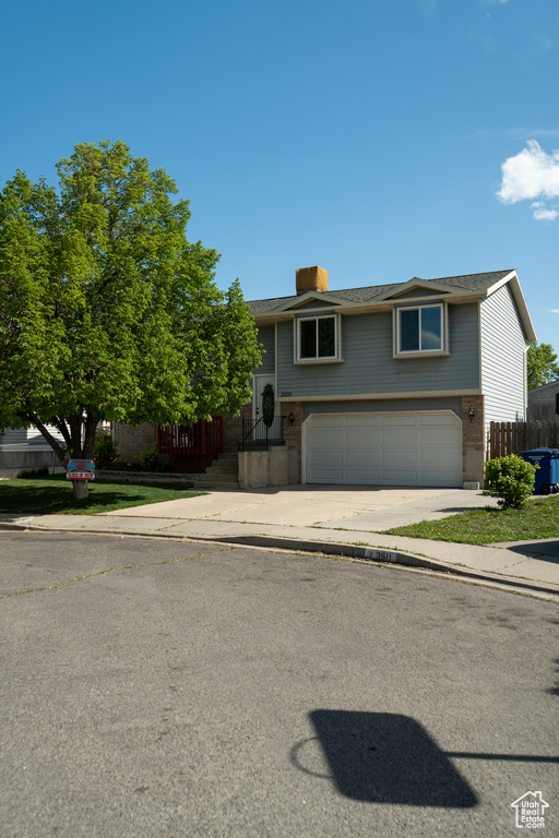 Raised ranch featuring a chimney, brick siding, fence, concrete driveway, and an attached garage