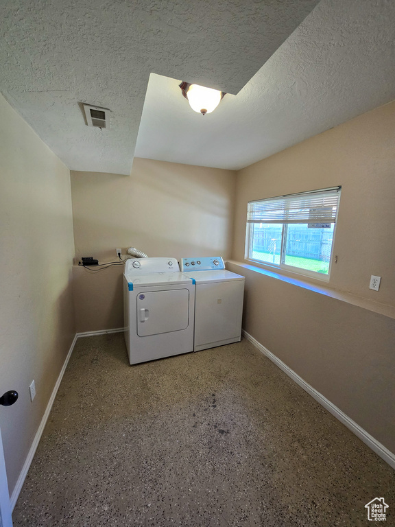 Clothes washing area featuring laundry area, baseboards, a textured ceiling, and washing machine and dryer
