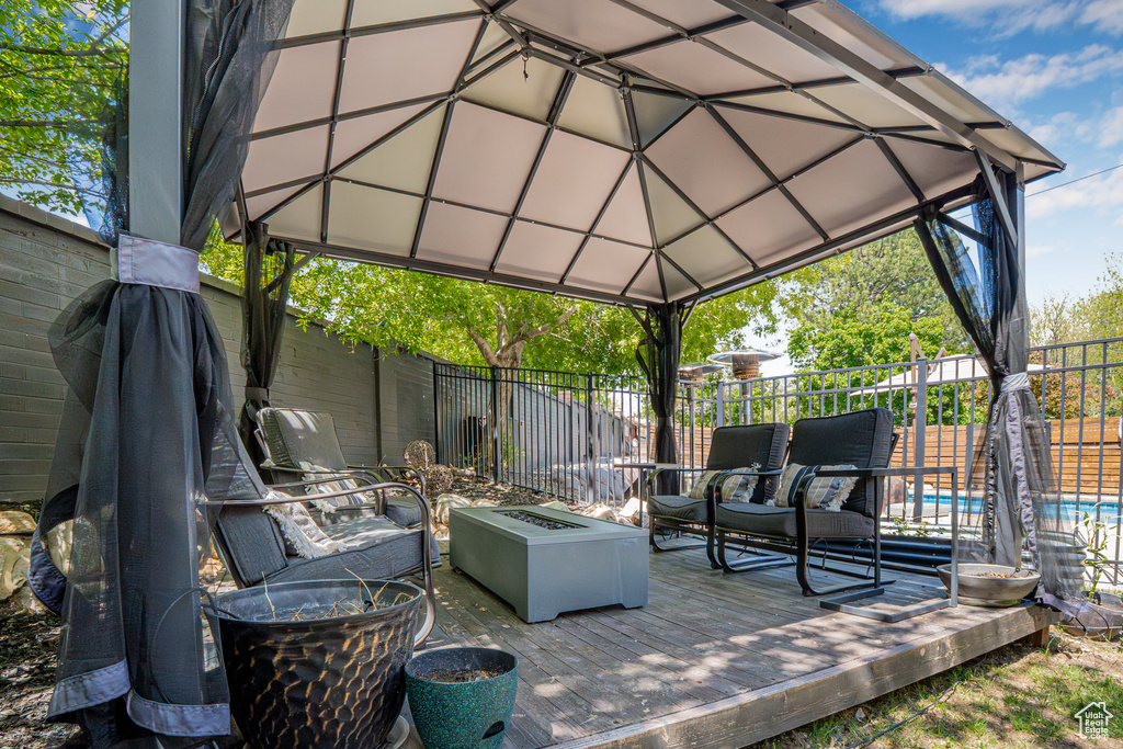 View of patio featuring a deck, a gazebo, a fenced in pool, a fenced backyard, and an outdoor living space with a fire pit