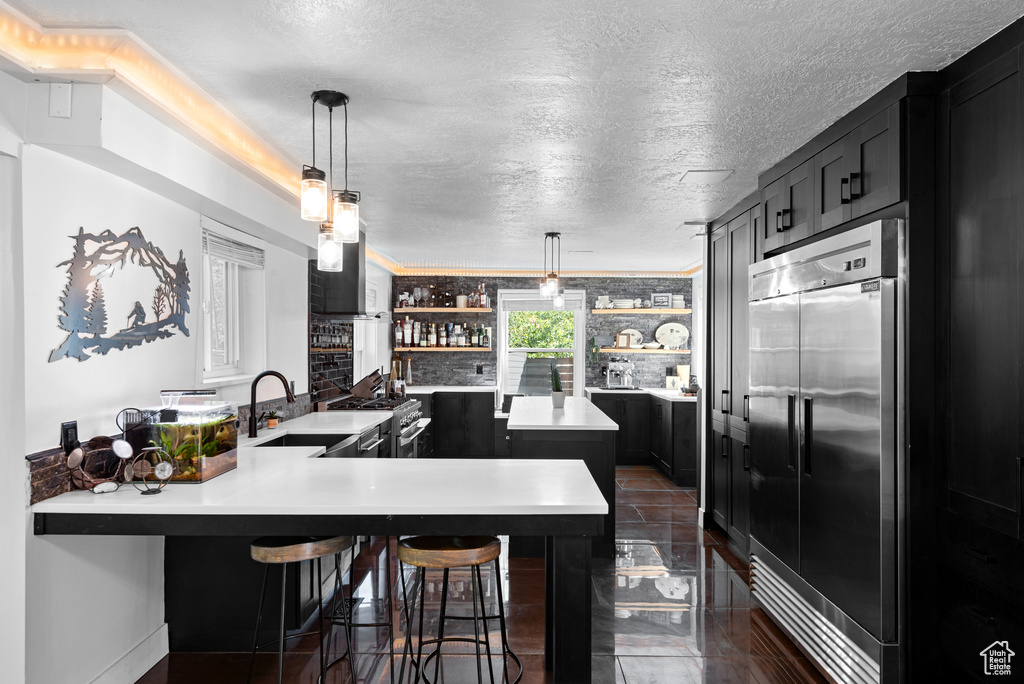 Kitchen with high end appliances, a sink, open shelves, light countertops, and dark cabinets