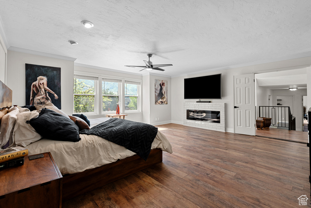 Bedroom featuring ornamental molding, a textured ceiling, wood finished floors, baseboards, and a glass covered fireplace