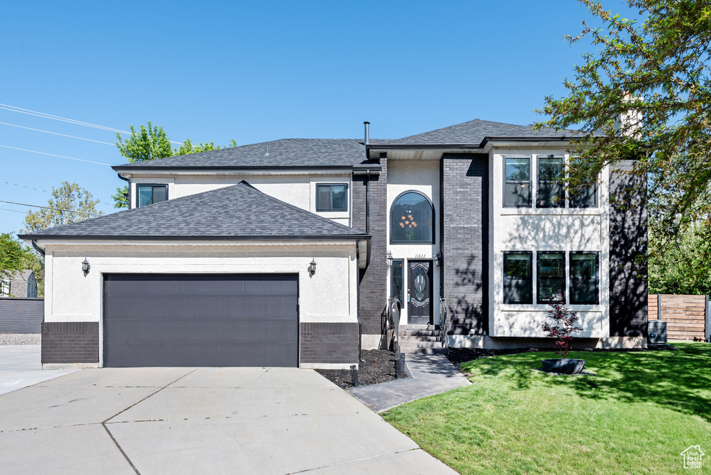 View of front of house featuring an attached garage, driveway, a front yard, and roof with shingles