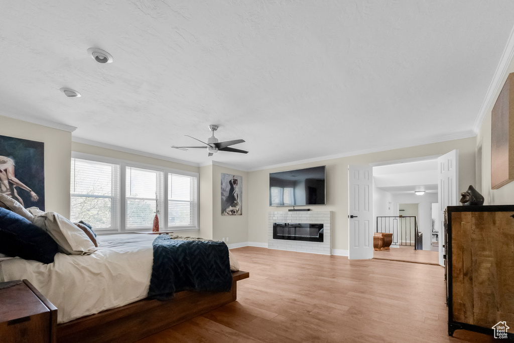 Bedroom featuring ornamental molding, a glass covered fireplace, wood finished floors, baseboards, and a ceiling fan