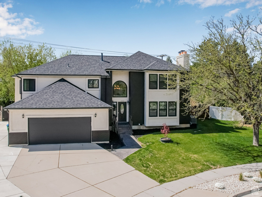 Traditional home with a front lawn, stucco siding, a shingled roof, concrete driveway, and an attached garage