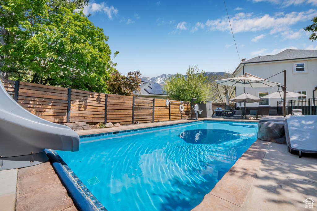 View of pool featuring a water slide, a fenced backyard, a fenced in pool, a mountain view, and a patio