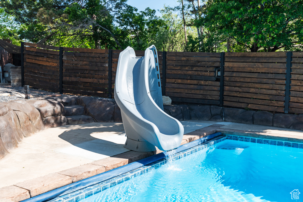 View of pool featuring a water slide, view of scattered trees, and a patio