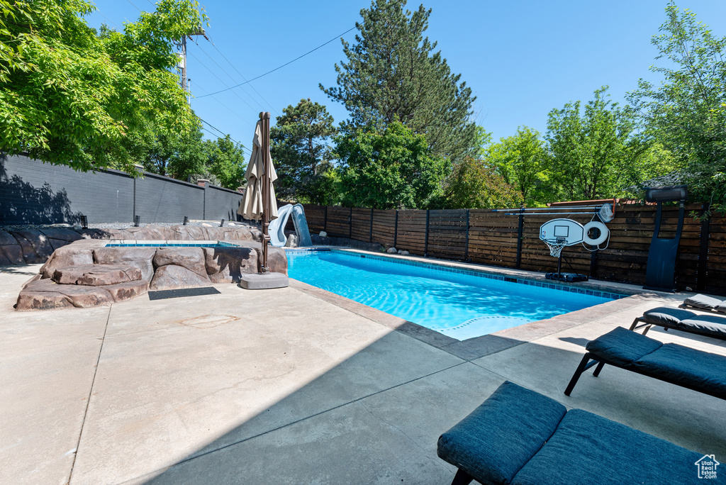 View of pool with a water slide, a fenced backyard, and a patio