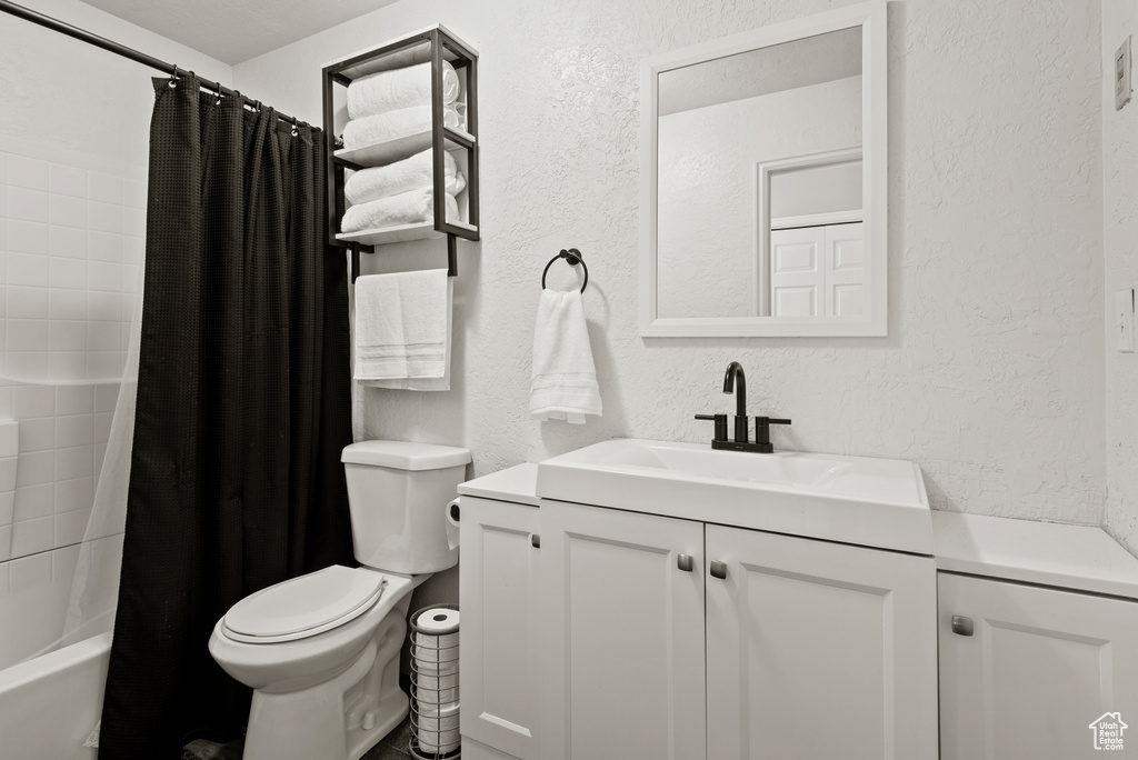 Bathroom featuring a textured wall, vanity, toilet, and shower / bathtub combination with curtain