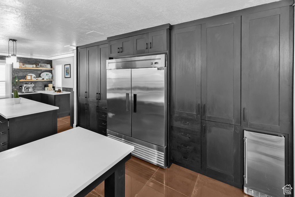 Kitchen with light countertops, a textured ceiling, stainless steel built in fridge, and open shelves