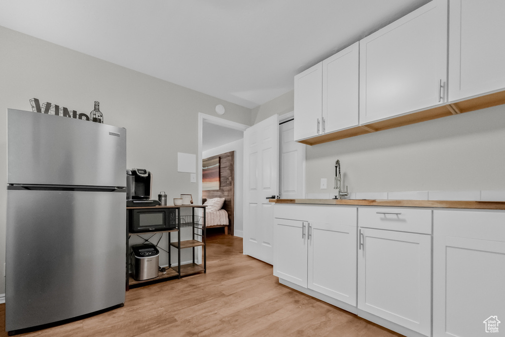 Kitchen featuring white cabinets, black microwave, a sink, freestanding refrigerator, and light wood-type flooring