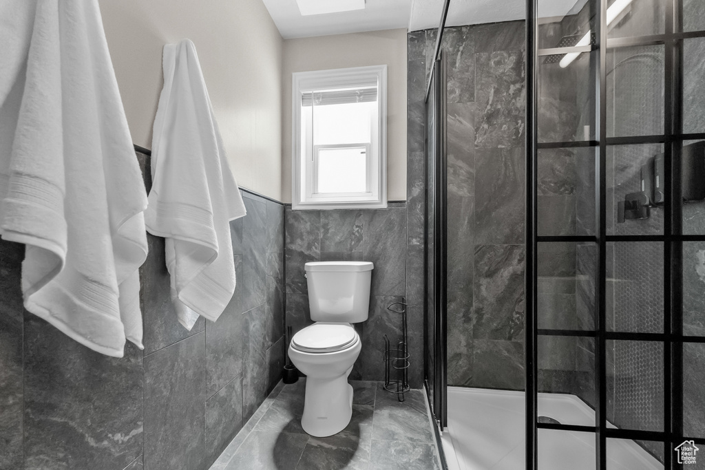 Bathroom featuring tile walls, a shower stall, toilet, and marble finish floor