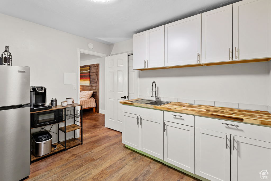 Kitchen with freestanding refrigerator, a sink, light wood-style flooring, butcher block countertops, and white cabinetry