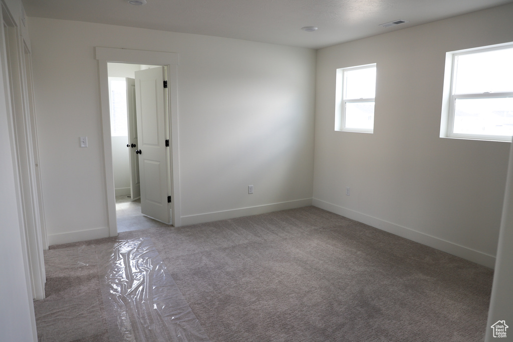 Empty room featuring baseboards, visible vents, and light colored carpet