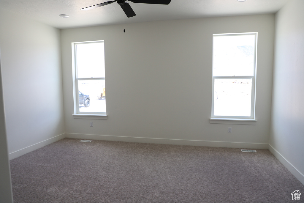 Carpeted empty room with ceiling fan, visible vents, and baseboards