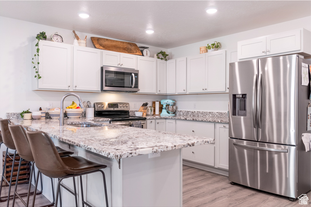 Kitchen featuring a peninsula, light stone countertops, a sink, light wood finished floors, and stainless steel appliances