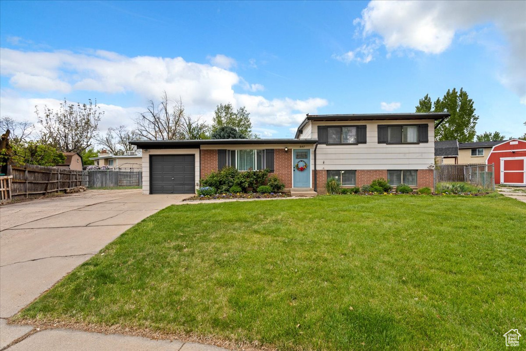 Tri-level home featuring a garage, a front lawn, fence, brick siding, and concrete driveway
