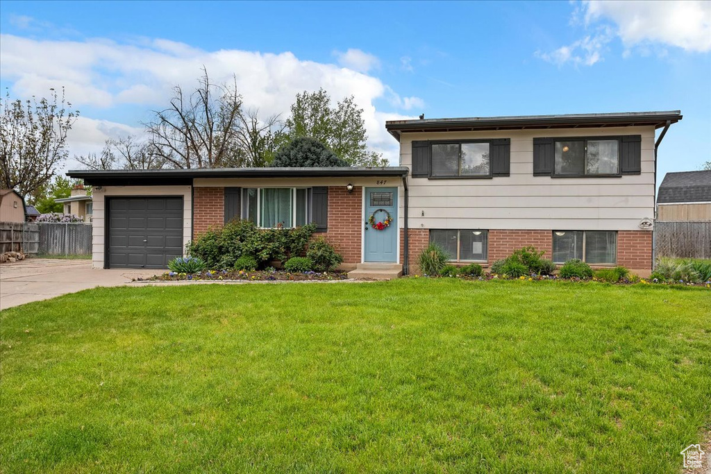 Tri-level home featuring fence, brick siding, a garage, a front yard, and driveway