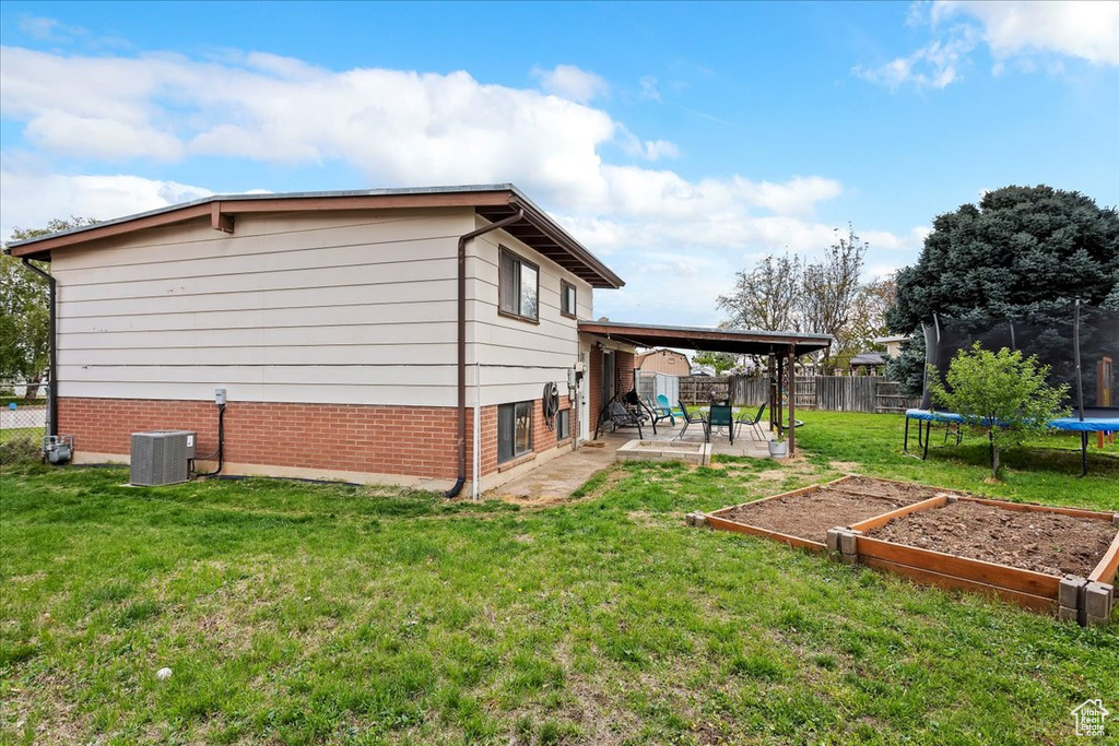 View of home's exterior with a trampoline, brick siding, a fenced backyard, a patio area, and a lawn