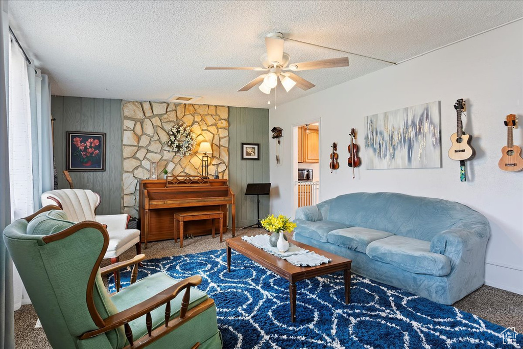 Living room featuring carpet floors, ceiling fan, visible vents, and wood walls