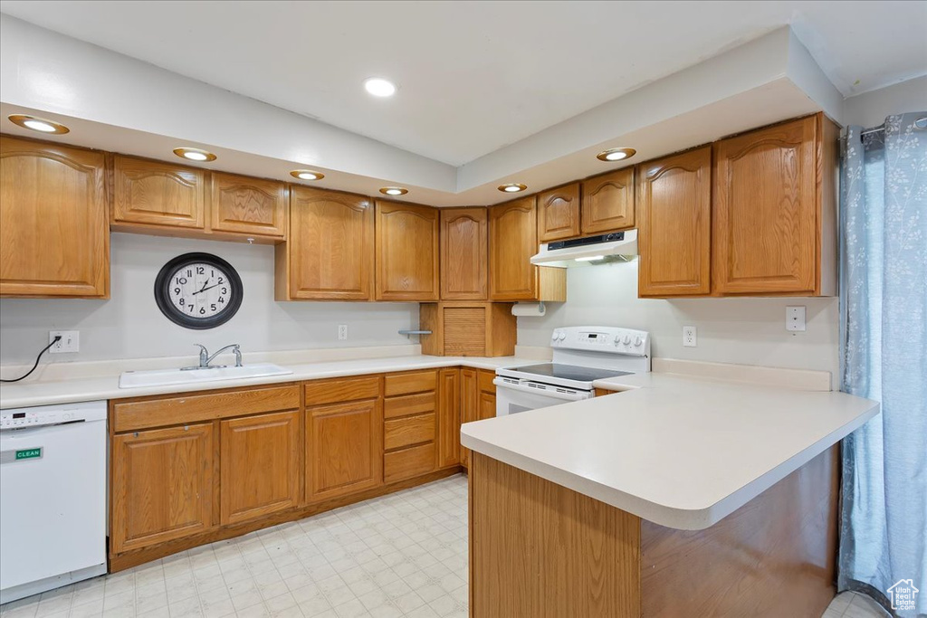 Kitchen with a sink, light countertops, a peninsula, under cabinet range hood, and white appliances