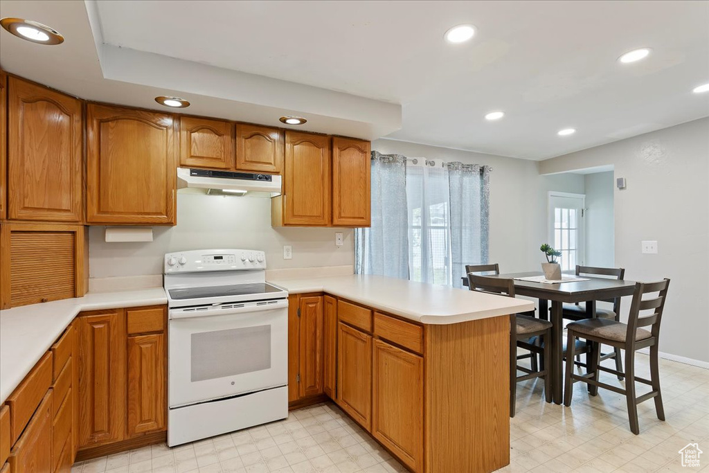Kitchen with light floors, white electric stove, a peninsula, and under cabinet range hood