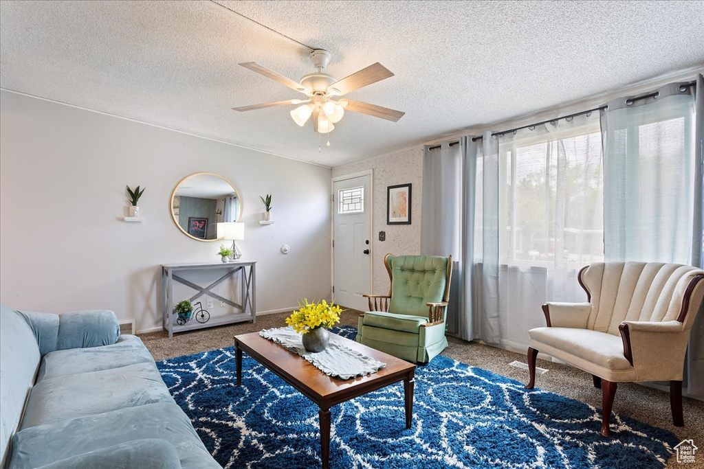 Carpeted living room with a ceiling fan, a textured ceiling, and baseboards