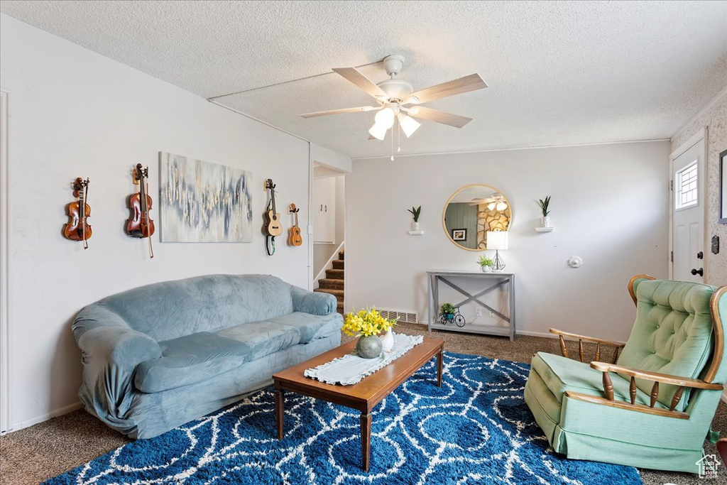 Carpeted living room featuring a textured ceiling, a ceiling fan, baseboards, visible vents, and stairway