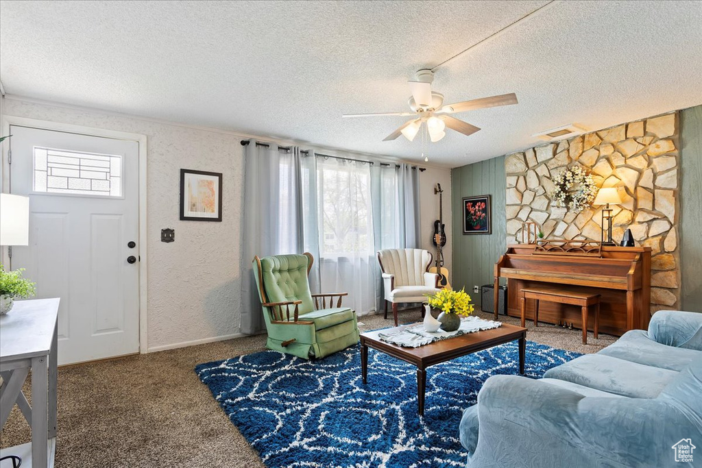 Carpeted living room with visible vents, a textured wall, baseboards, ceiling fan, and a textured ceiling