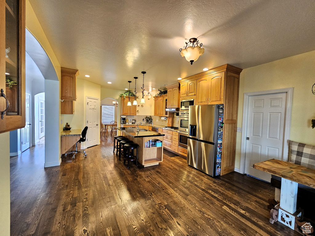 Kitchen featuring dark wood-style flooring, a kitchen bar, a center island, arched walkways, and appliances with stainless steel finishes