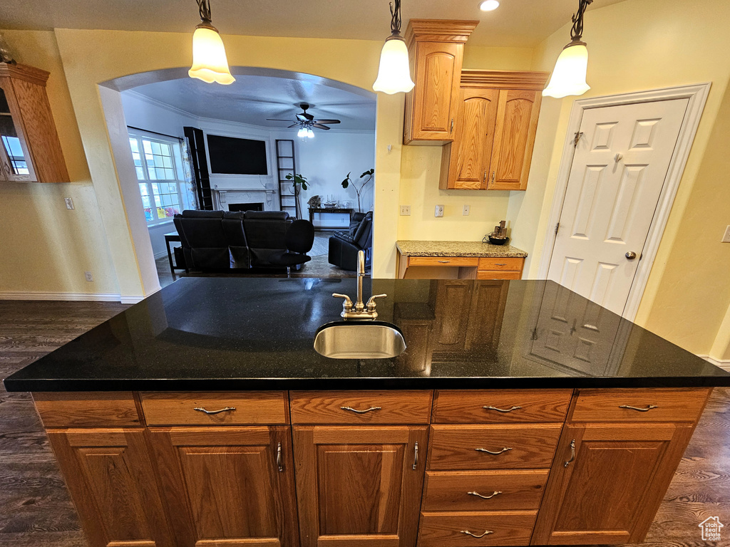 Kitchen with a ceiling fan, a fireplace, arched walkways, a sink, and dark wood finished floors