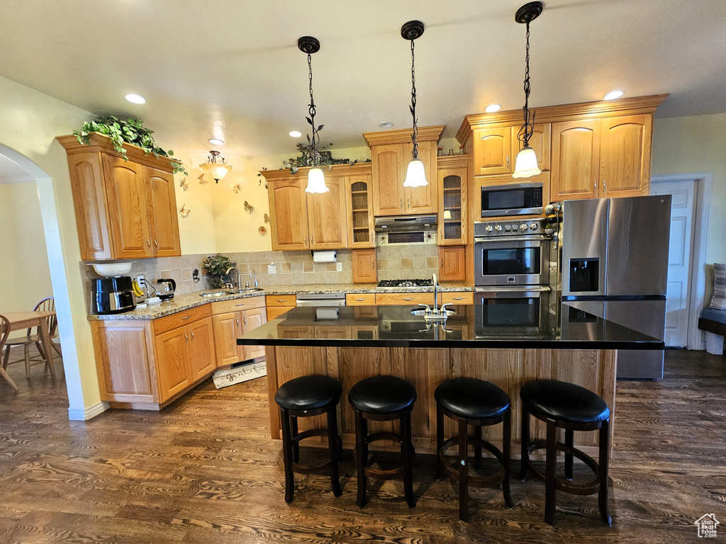 Kitchen featuring an island with sink, a breakfast bar area, range hood, arched walkways, and appliances with stainless steel finishes