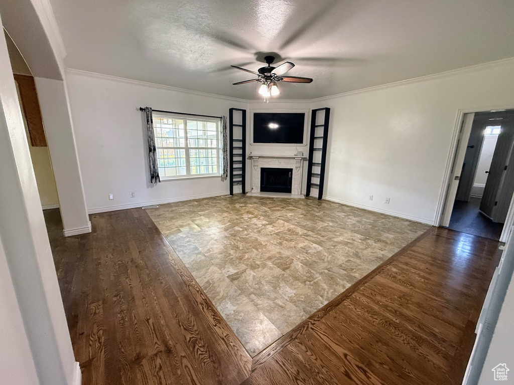 Unfurnished living room featuring a ceiling fan, ornamental molding, a fireplace, wood finished floors, and baseboards