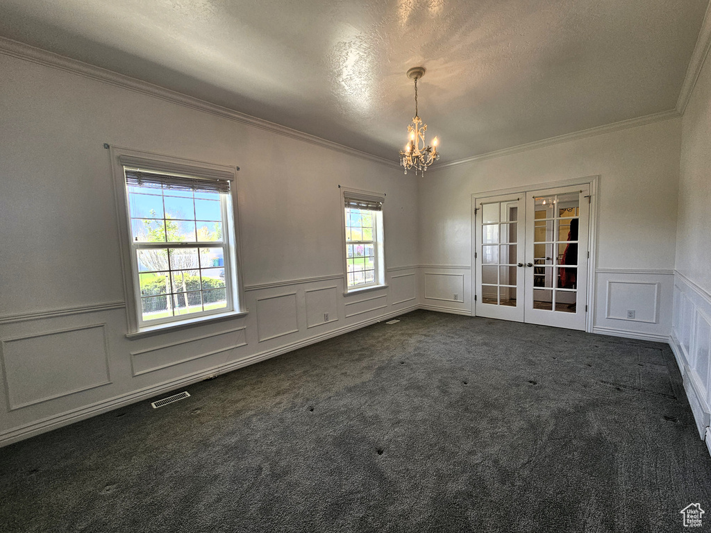Spare room with crown molding, a decorative wall, dark colored carpet, french doors, and a notable chandelier