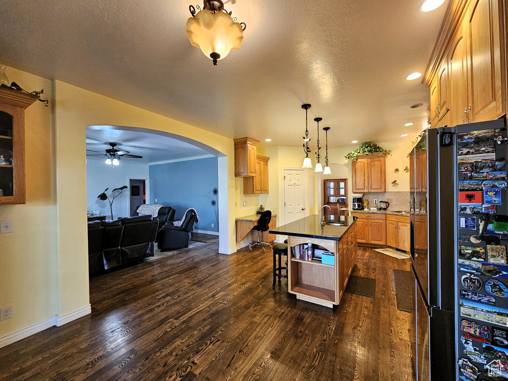Kitchen with ceiling fan, dark wood-style flooring, arched walkways, baseboards, and freestanding refrigerator