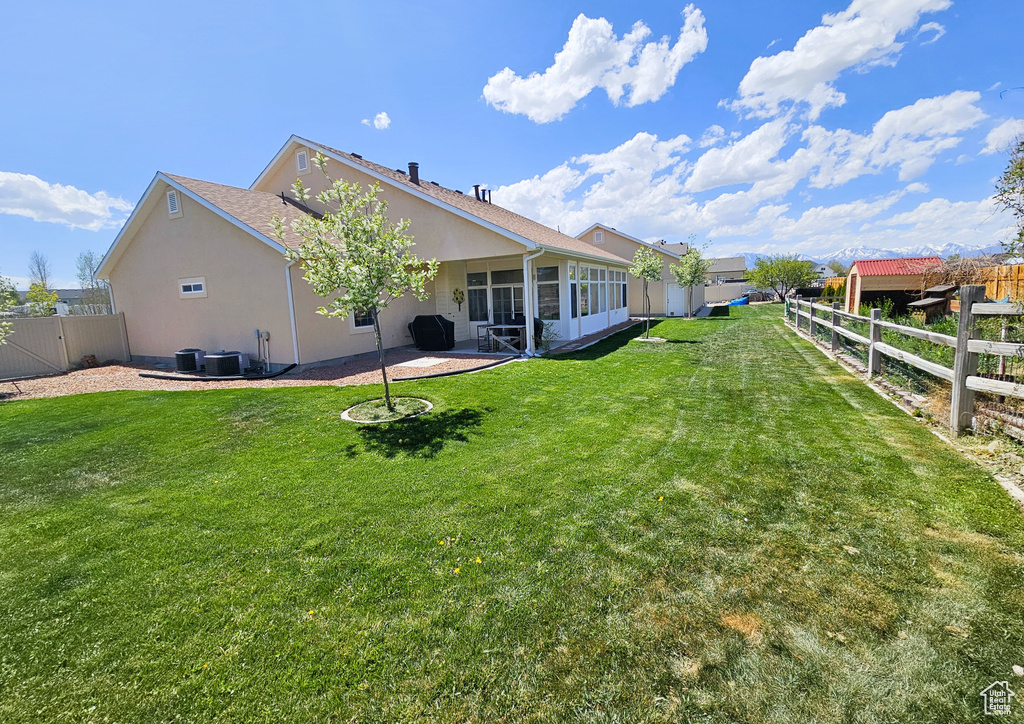 Back of house featuring a patio, a fenced backyard, stucco siding, a sunroom, and a yard